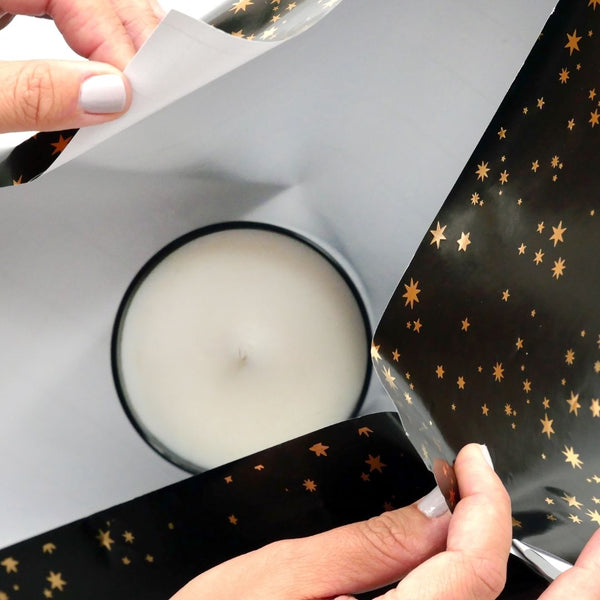 Hands wrapping a candle in dark star-patterned gift paper