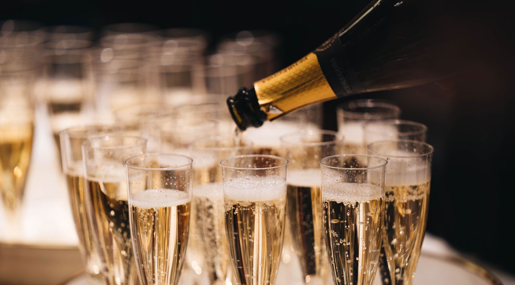 Champagne being poured into rows of sparkling glass flutes