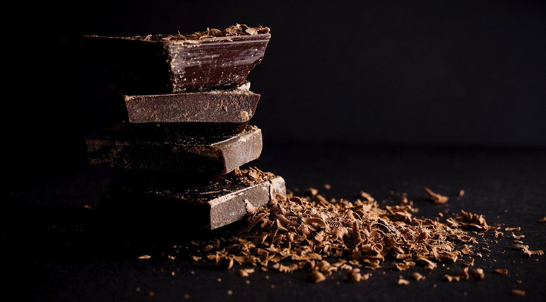 Stack of dark chocolate pieces with cocoa shavings on dark background