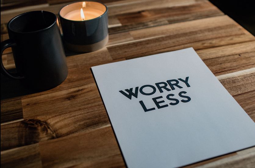 Lit candle beside a black mug and Worry Less card on wood