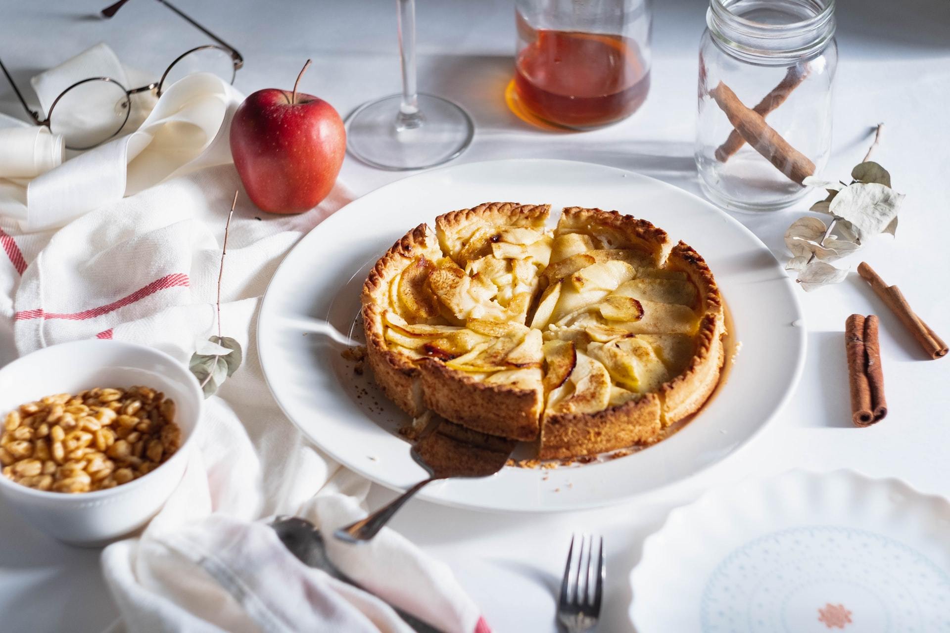 Apple tart on white plate with apples, cinnamon sticks and nuts
