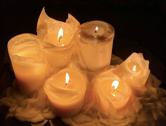 Several lit candles burning down with melting wax in the dark