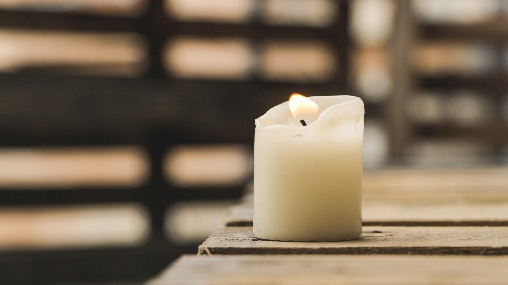 Single white pillar candle on a wooden surface with blurred background
