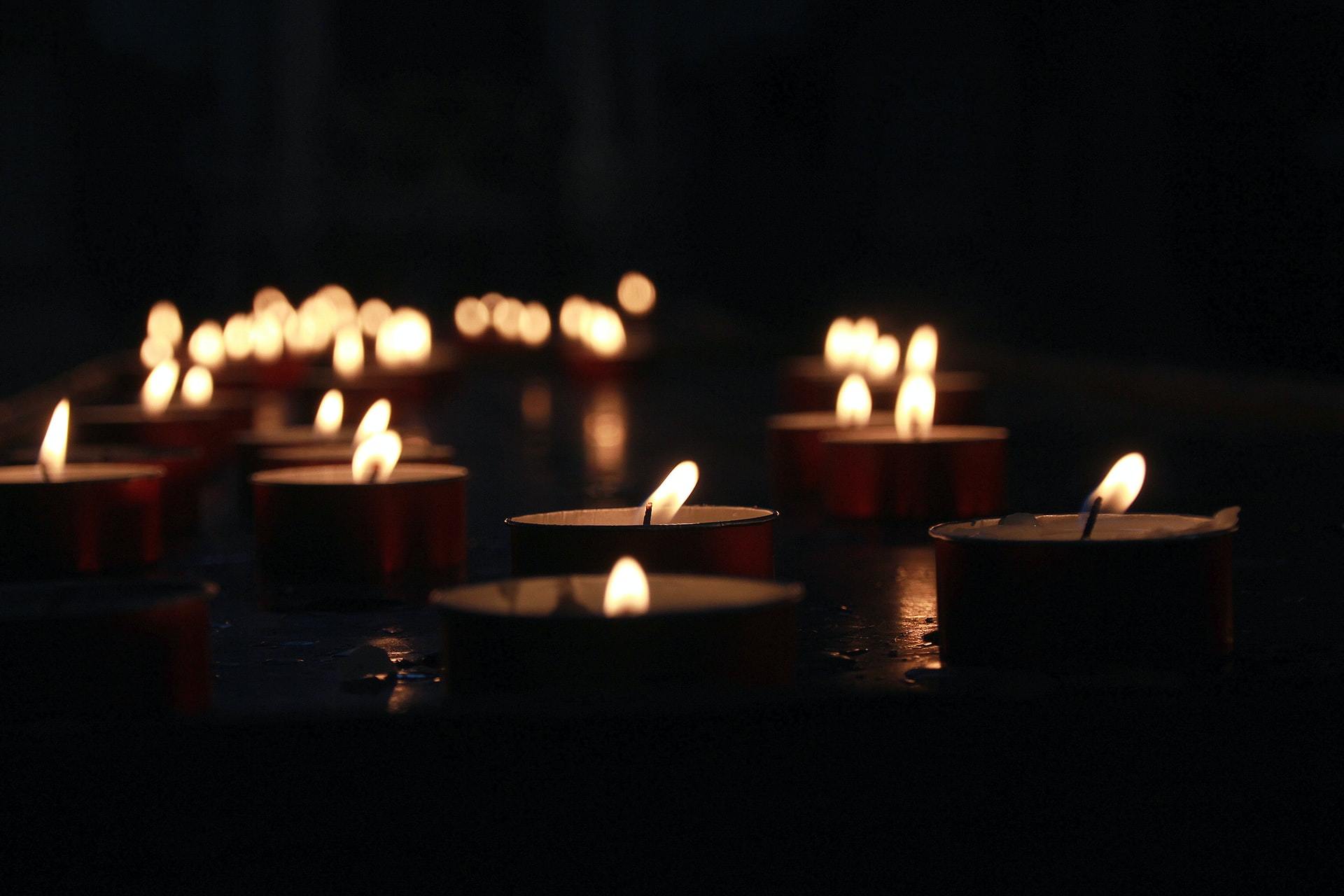 Many small lit tea light candles glowing in the dark