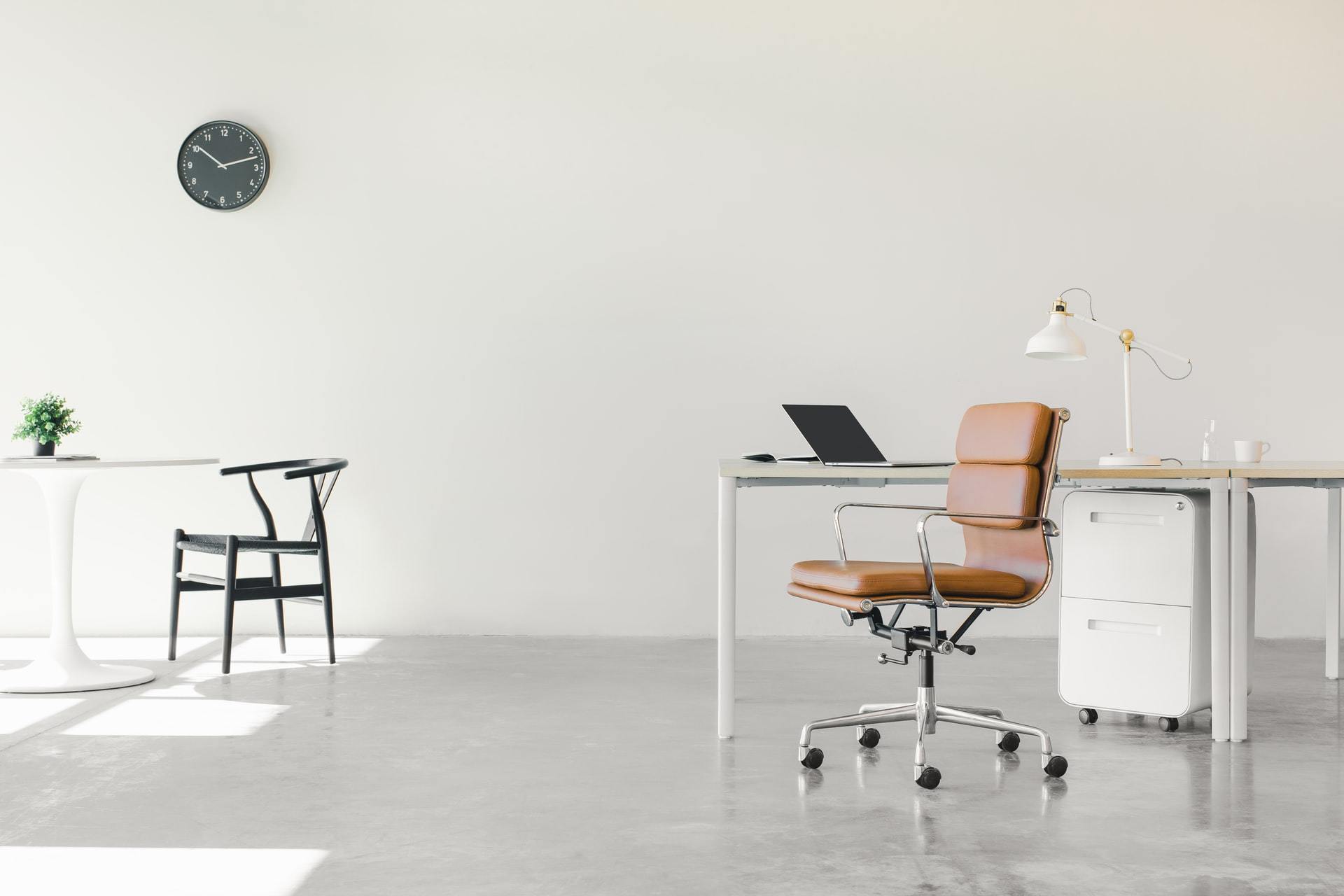 Minimalist bright home office with white desk, leather chair and laptop