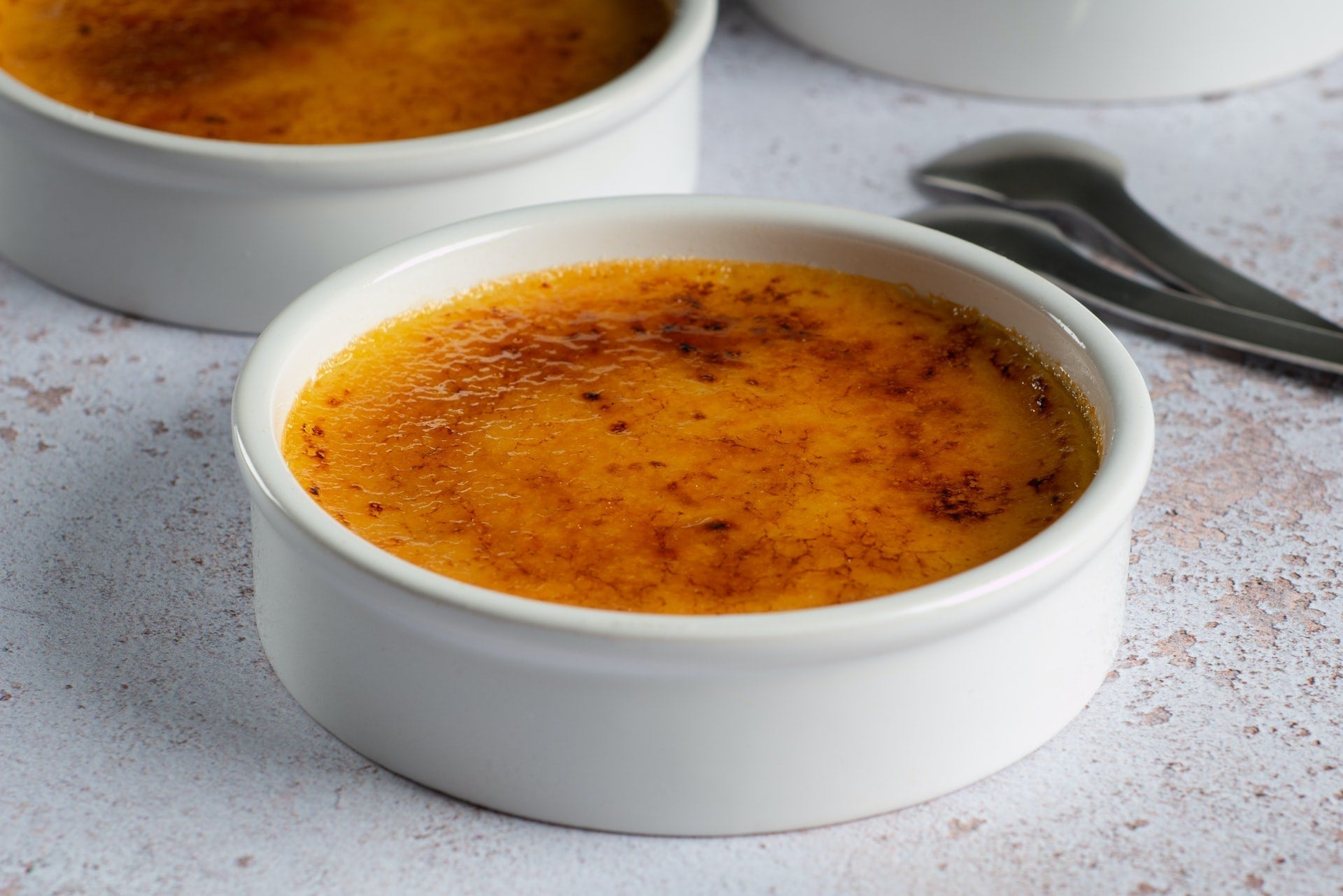 Ramekins of crème brûlée with caramelized tops and a spoon