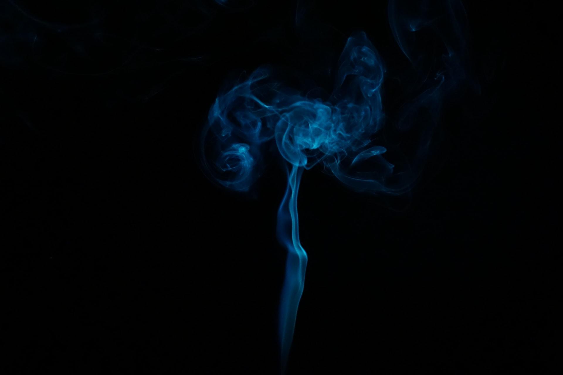 Wisps of smoke rising from an extinguished candle against black background