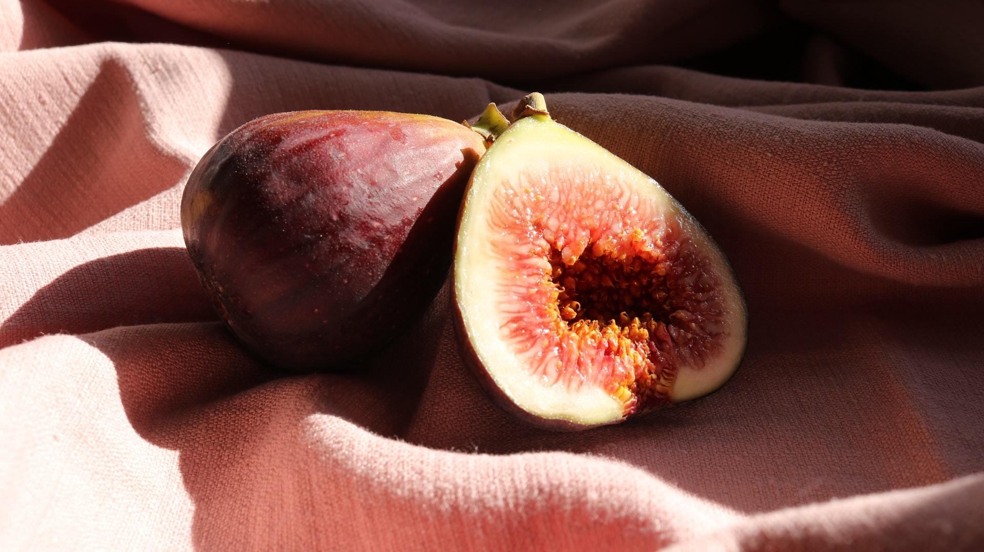 Fresh figs with one halved showing pink interior on draped fabric
