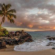 Tropical Pacific beach with palm trees and rocky shore at sunset